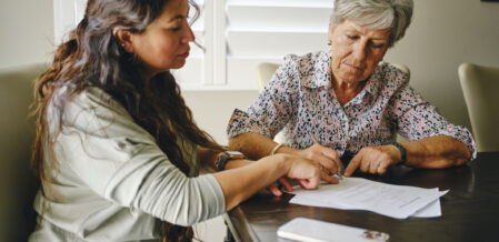 A Hispanic woman, helping a senior aged woman prepare financial documents.