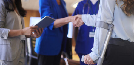 Woman injured in a car accident using a crutch shakes hands with an attorney in a blue blazer with two other attorneys standing next to them.