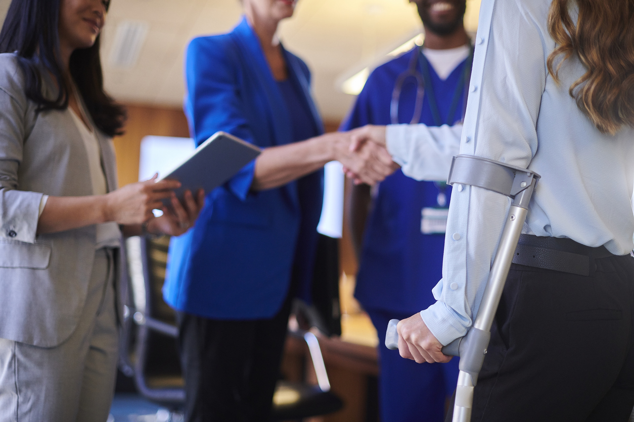 Woman injured in a car accident using a crutch shakes hands with an attorney in a blue blazer with two other attorneys standing next to them.