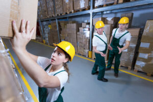 Young afraid woman lifting heavy box in warehouse