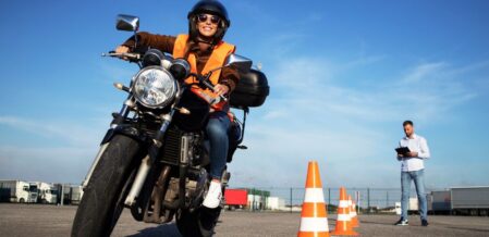 Image of a man writing a motorcycle around orange cones while a man with a clipboard watches on