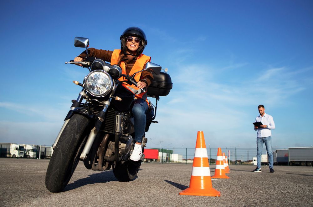 Image of a man writing a motorcycle around orange cones while a man with a clipboard watches on