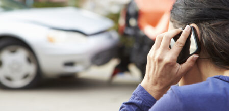 Image of someone on the phone while looking at a damaged car