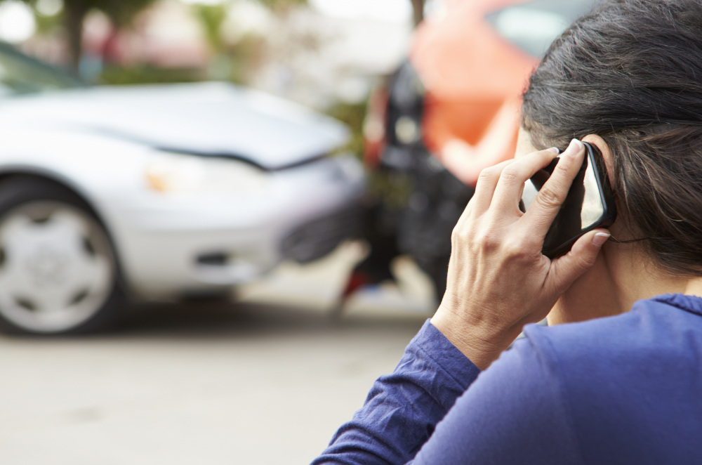 Image of someone on the phone while looking at a damaged car