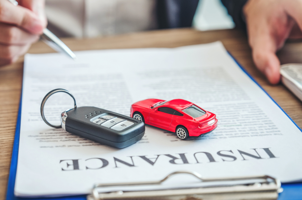 Image of a small toy car and a key fob on top of an auto insurance form