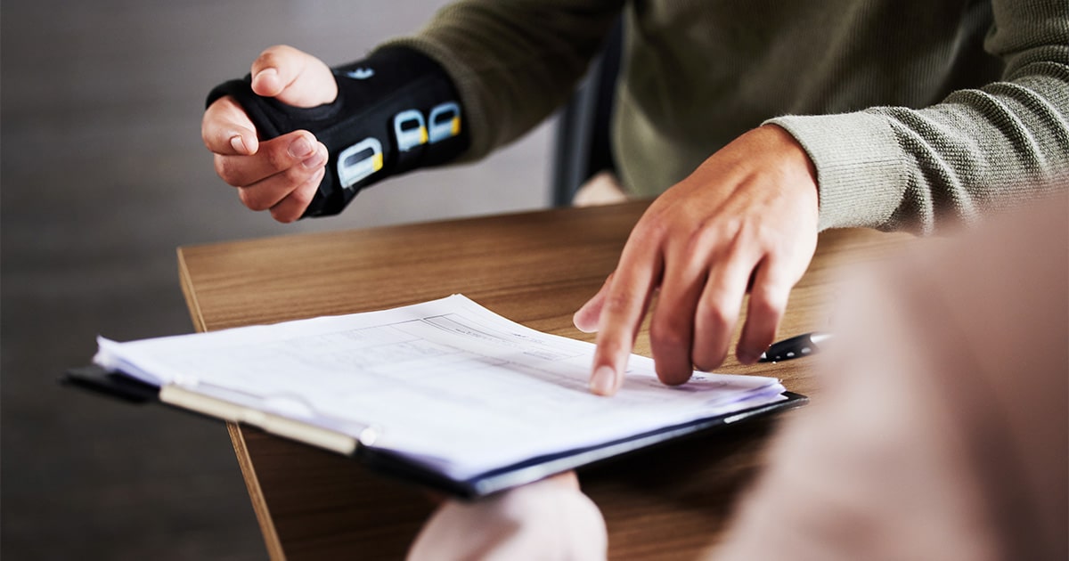 Person with their wrist in a brace pointing at paperwork