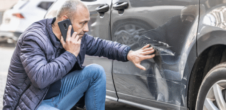 a man inspecting the scratch along the side of his car while on the phone