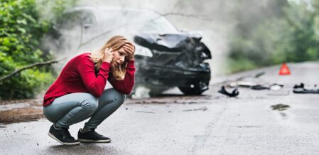 girl on the phone panicked standing beside her wrecked car