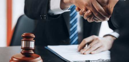 two men shaking hands with a gavel sitting on the desk between them
