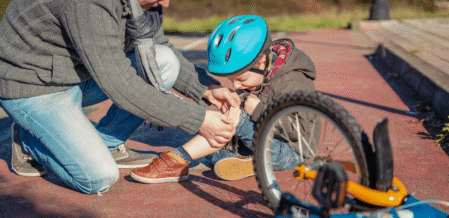 Image of a dad helping his daughter put a bandage on a scraped knee after a fall from a bicycle
