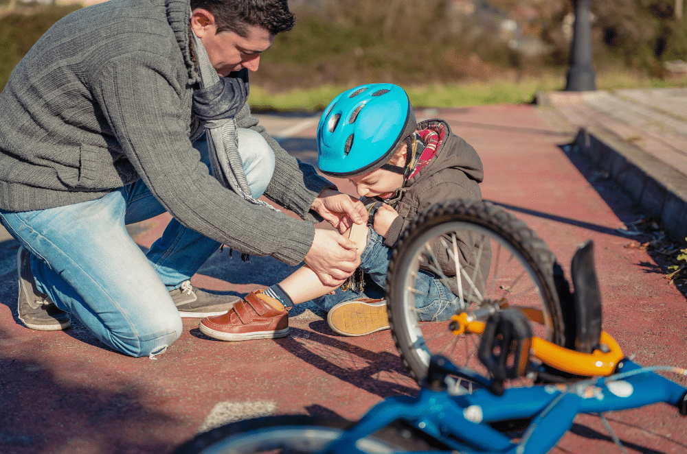 Image of a dad helping his daughter put a bandage on a scraped knee after a fall from a bicycle