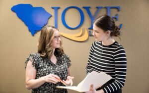 two women talking over a file in front of the Joye Law Firm sign