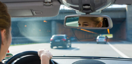 Lady driving a car about to go under a bridge. See her through the review mirror