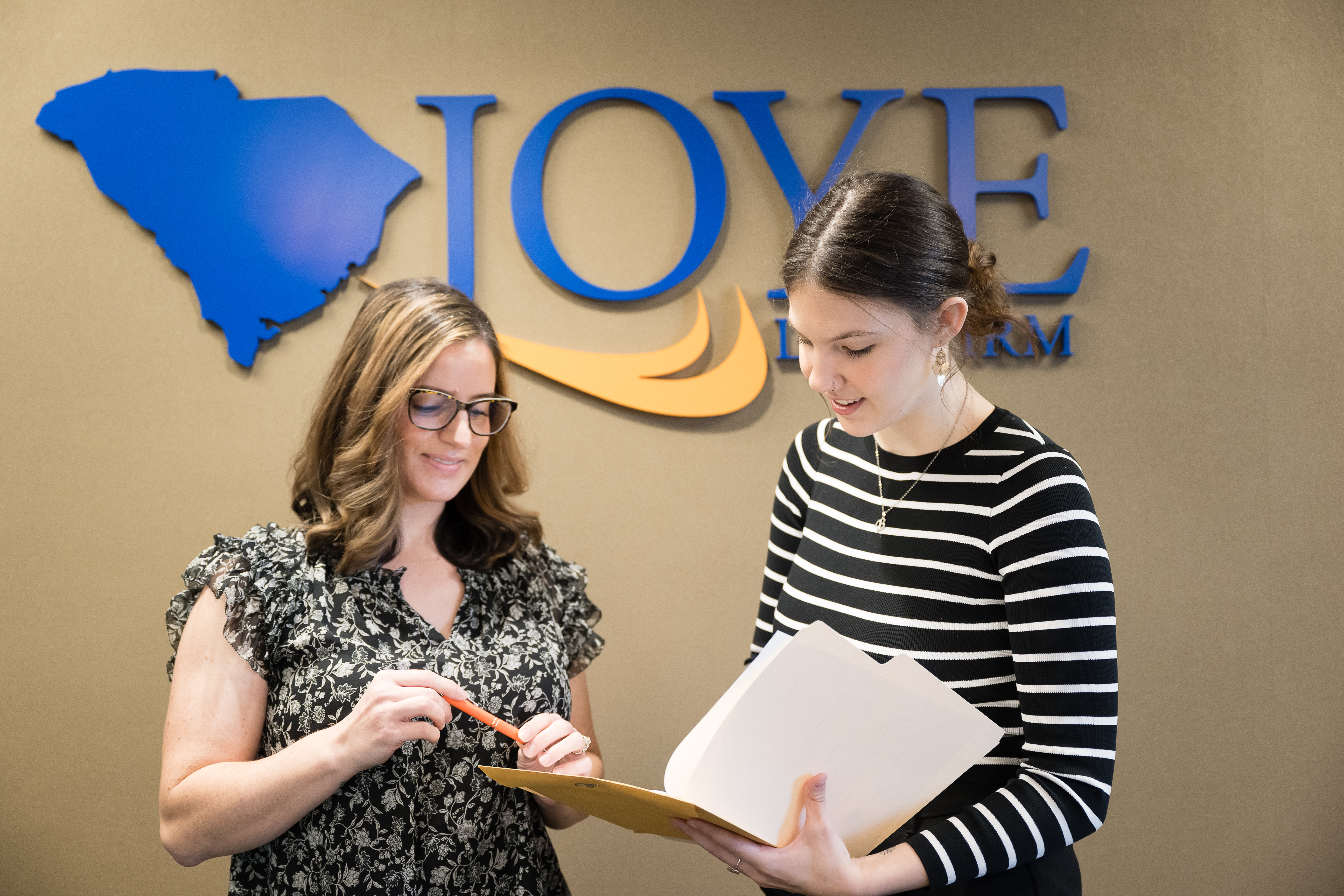 Women standing in front of the Joye Law Firm sign talking over a folder