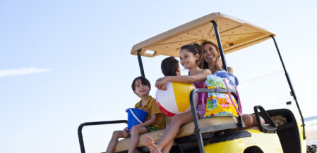 Smiling family of four rides a golf cart down the beach in South Carolina, enjoying a peaceful family golf cart ride