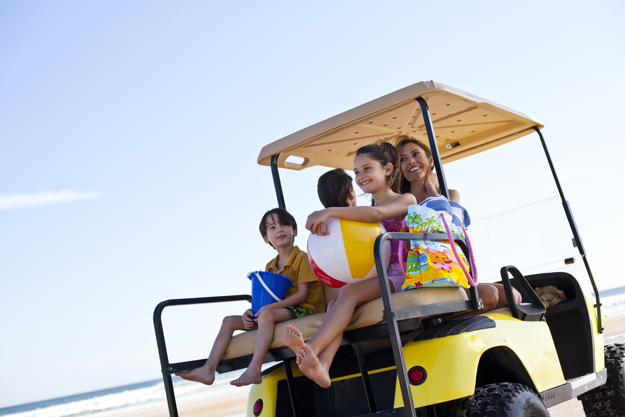 Smiling family of four rides a golf cart down the beach in South Carolina, enjoying a peaceful family golf cart ride