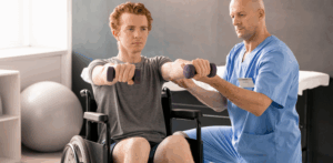 Physical therapist assisting a young man in a wheelchair with arm exercises using small purple dumbbells