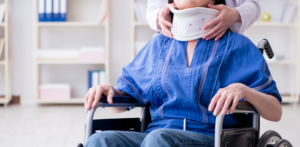Woman in wheelchair receives help adjusting a neck brace in a medical or rehab setting