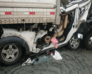 Picture of a car crushed between two 18-wheeler trucks.