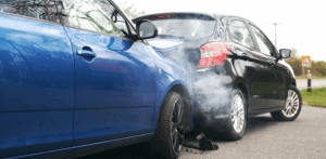 Rear-end collision between blue and black cars with visible smoke and bumper damage on a street