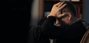 Stressed man sits with head in hands, overwhelmed by emotional or mental distress in a dim room