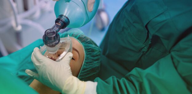 Anesthesiologist holding an anesthesia mask over a patient's face during surgery
